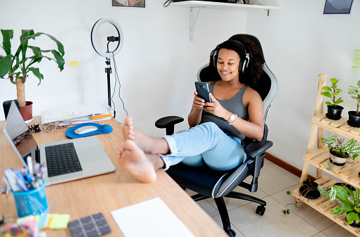 Young woman wearing headphones watching a video streaming on her laptop while sitting in her home office