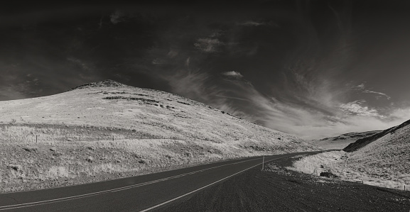 infrared image of a road disappearing into the distance between two hills
