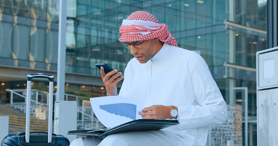 Arab business man, phone call on speaker with folder, communication and technology in city and company travel. Virtual meeting, paperwork and project strategy, Muslim person and networking with 5g