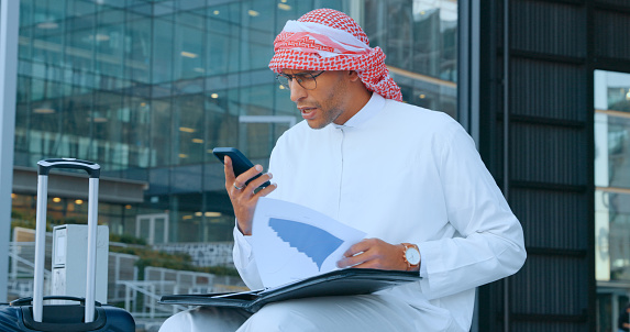 Arab business man, phone call on speaker with folder, communication and technology in city and company travel. Virtual meeting, paperwork and project strategy, Muslim person and networking with 5g