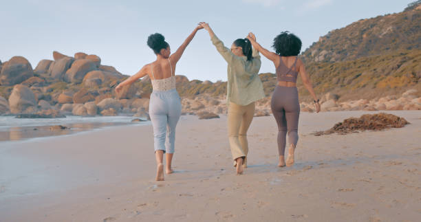 Holding hands, friends or walking at a beach for holiday vacation while bonding or laughing together. Happy people with women group relaxing at seashore on an ocean trip in Miami
