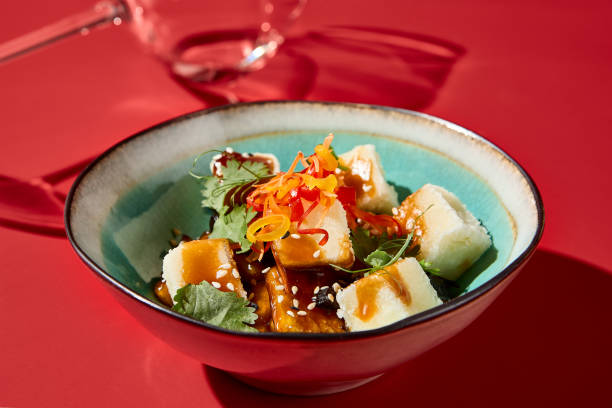 salada de berinjela-tofu em uma tigela de cerâmica, estilo asiático, contra um fundo de veludo vermelho escuro, taça de vinho ao fundo - 16192 - fotografias e filmes do acervo