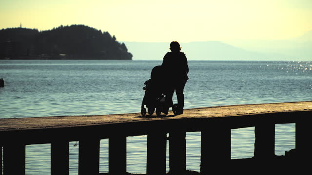 Young mother walking enjoying on the pier with her baby in a stroller at sunset