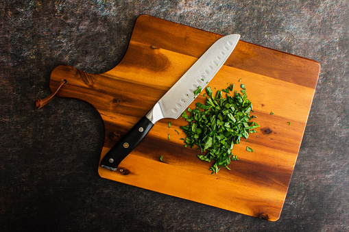 Chopped Basil with a Chef's Knife on a Wooden Cutting Board: Prepped Genovese basil leaves on a wood chopping board with a santoku knife