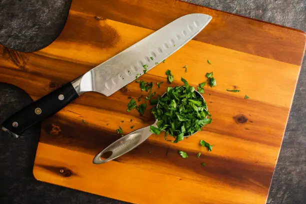 Prepped Genovese basil leaves on a chopping board with a santoku knife