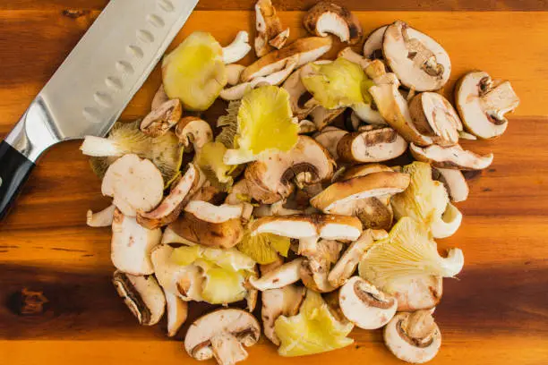 Prepped oyster, shiitake, and crimini mushrooms piled up on a chopping board