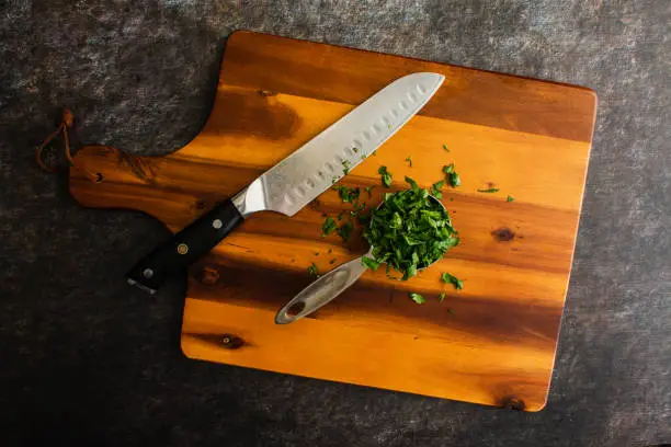 Prepped Genovese basil leaves on a chopping board with a santoku knife