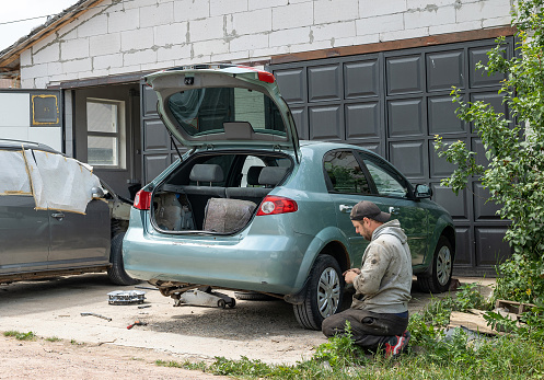 Auto repair shop with broken cars. The professional auto mechanic changes the rear right wheel of the car.