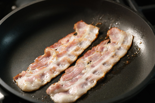 bacon stripes in frying pan closeup, shallow focus