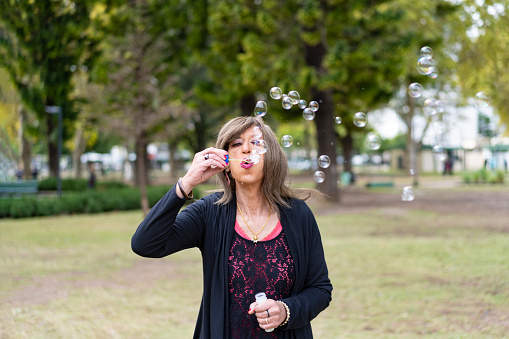 Mature trans woman blowing bubbles in a park