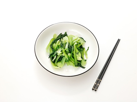 An overhead view of a white surface with a bowl of pickled cucumbers and chopsticks arranged neatly in the center