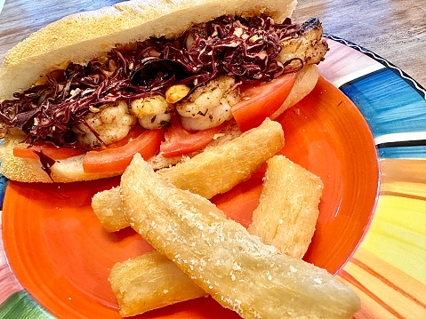 Blackened shrimp po’boy sandwich with Asian Slaw, tomato, cheese and Yum Yum sauce and a side of yucca fries.