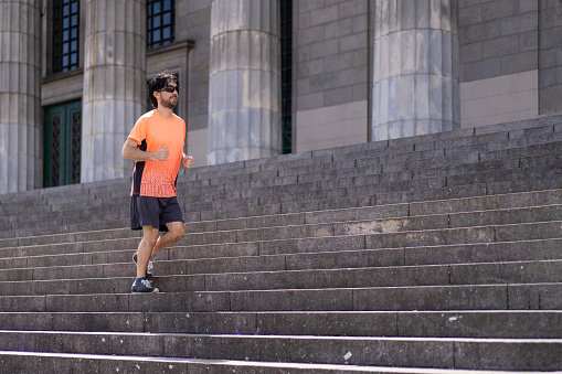 Portrait of handsome attractive mature bearded athletic latin man guy 40s in orange t-shirt running on some stairs.