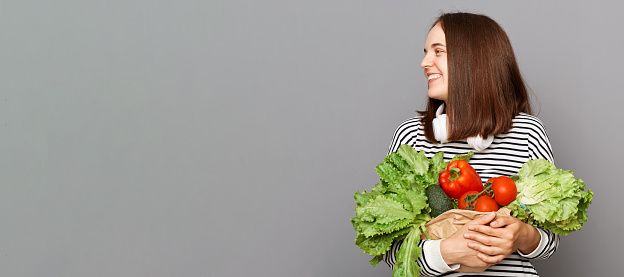 Vegetarian lifestyle nourish and thrive. Fresh and organic key to wellness fueled by nutritious food. Joyful woman holding vegetables isolated over gray background, copy space for advertisement.