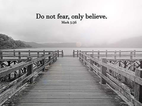 Bible verse quote - Do not fear, only believe. Mark 5:36. Christianity bible verses concept with empty wooden bridge and light on a foggy and rainy day in black and white vintage art background.