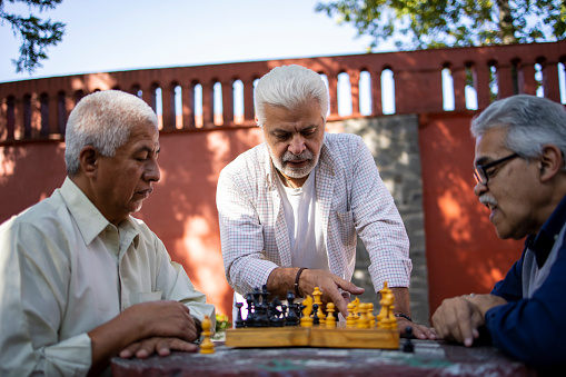 Three senior Latin friends playing chess at the park