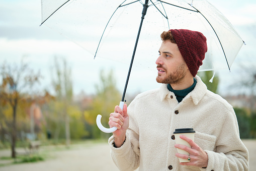 Young man with a coffee and transparent umbrella in street in winter.