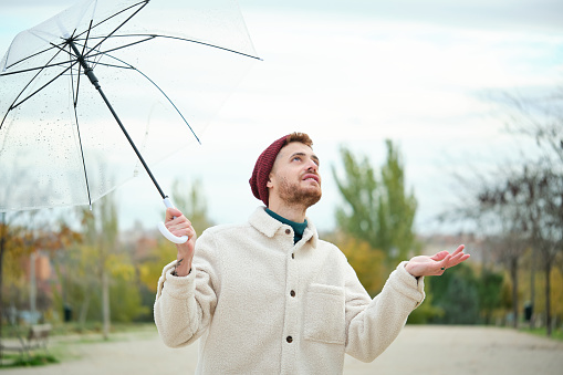 Young man with a transparent umbrella checking if it is raining in street in autumn.