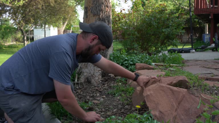 Close Up of a White Man in his Thirties Pulling Weeds in his Backyard on a Sunny Day