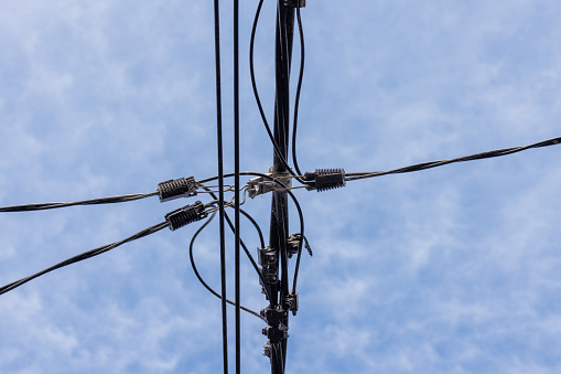 Electrical telephone wires against a cloudy blue sky.