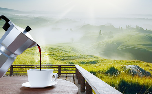 Pour fresh coffee from the Mocha pot into the red coffee mug. There is smoke rising from the hot coffee. Red glasses on a wooden table top. The background is mountain scenery. The morning sun, there is a thin mist above the ground. 3D Rendering