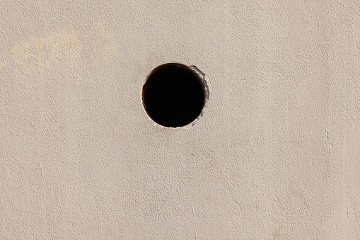 Part of an old painted concrete wall with drainage hole.