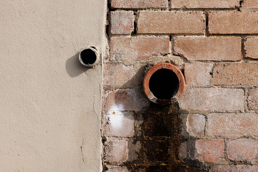 Two drainage pipes on beige and brick walls with water stains.
