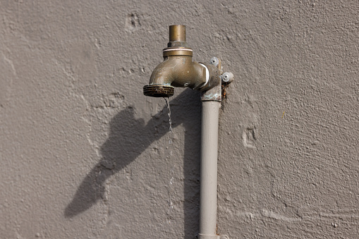 Leaking faucet against a wall in the sun with shadow.