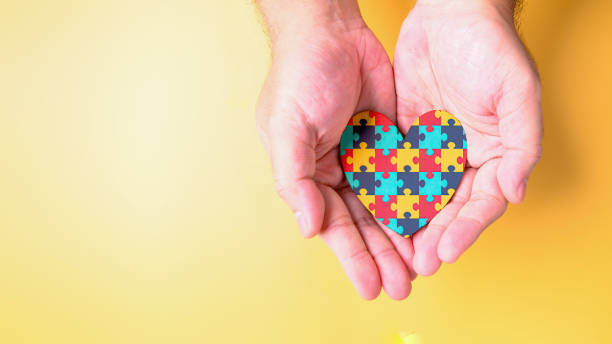 Adult hands holding multicolor jigsaw puzzle inside the heart shape. Autism awareness and Autism spectrum disorder syndrome healthcare family support concept. World Autism Awareness Day symbol theme stock photo