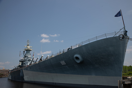 The forward turret and 5 inch Mk45 Mod 2 automatic rapid fire gun of HMAS Arunta, an Anzac Class frigate of the Royal Australian Navy.  She is docked at Garden Island, Sydney Harbour. In the background is a pole with six visible security cameras. This image was taken on a hot and sunny afternoon from Woolloomooloo Bay on 3 March 2024.