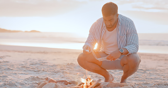 Bonfire, beach and man lighting fire for a picnic for summer holiday vacation at sunset. Travel, freedom or person relaxing on seashore on ocean trip in Miami, Florida