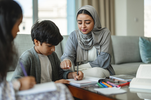 Middle eastern mother helping her son with school work while her daughter is listening to her. Focus is on mother.