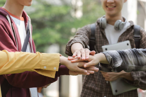istock A group of diverse, multiracial young people are shown happily stacking their hands together while standing outside a building. This represents a sense of unity, fun,relationship and youth culture. 1497319650
