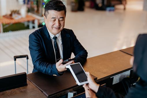 An Asian Chinese businessman making contactless payment with smartphone at hotel reception. smartphone contactless payment concept.