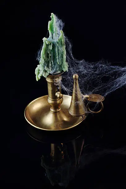 A brass candlestick covered with a cobweb, on black. Ideal for Halloween.