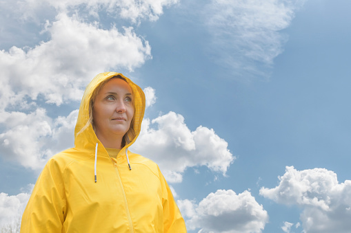 Portrait of a girl dressed in a yellow jacket with a hood on her head and looking into the distance against a cloudy sky. copy space