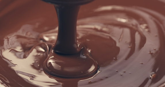 premium dark melted chocolate being poured from spoon closeup toned, 4k photo