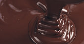 premium dark melted chocolate being poured from spoon in right part of frame from above toned