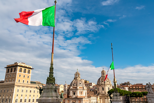 Italian national flag moving in wind with view on dome of Santa Maria di Loreto church and dome of Church of the Most Holy Name of Mary at Trajan Forum. Landmark in city of Rome, Lazio, Italy, Europe