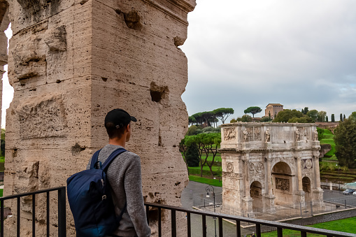 Tourist man wtith backpack enjoying the view from the interior of Colosseum on Triumphal Arch of Constantine in city of Rome, Lazio, Italy, Europe. UNESCO World Heritage Site. Tourism in European city