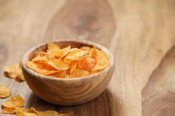potato chips with paprika in wood bowl on table, shallow focus