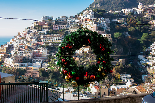 Christmas wreath with panoramic view on colorful houses of coastal town Positano, Amalfi Coast, Italy, Campania, Europe. Holiday decoration. Winter vacation at coastline Tyrrhenian, Mediterranean Sea