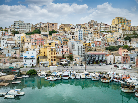 Sciacca City Marina and Sciacca Village Cityscape with residential houses built up to the hill under beautiful blue summer sky. Tourboats and Motorboats anchored in the Marina of the old Town. Sciacca, Agrigento, Sicily Island, Southern Italy, Southern Europe.