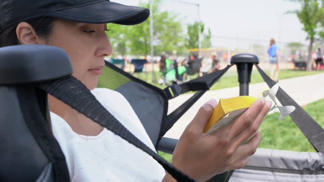 Close up Shot of a Black Female Reading a Book While Seating in a Chair on a Sunny Day