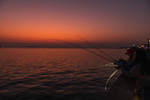 Seattle, USA - Oct 9th, 2022: A vivid sunset on Elliott bay off pier 62 as people fish in the unusually warm weather.