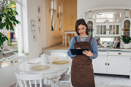 A waitress in an apron stands in a restaurant and writes down an order using a digital tablet