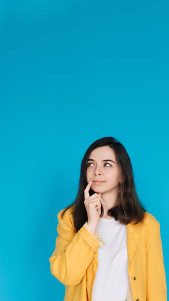 thoughtful and stylish woman in trendy clothing - portrait of an attractive young lady with a skeptical gaze, isolated on blue background - copy space available - bolero jacket imagens e fotografias de stock