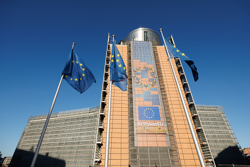 European flags in front of the Berlaymont building, headquarters of the European Commission in Brussels, Belgium. The Commission promotes the general interest of the EU by proposing and enforcing legislation as well as by implementing policies and the EU budget