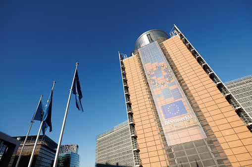 European flags in front of the Berlaymont building, headquarters of the European Commission in Brussels, Belgium. The Commission promotes the general interest of the EU by proposing and enforcing legislation as well as by implementing policies and the EU budget