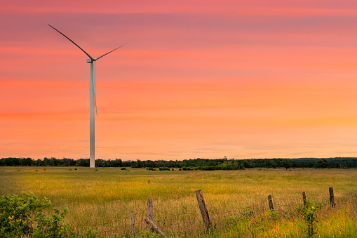 A electric generating wind turbine is prominently displayed in this rural agricultural landscape. It is during golden hour at sunset. This image is from Nipissing District in Ontario Canada.